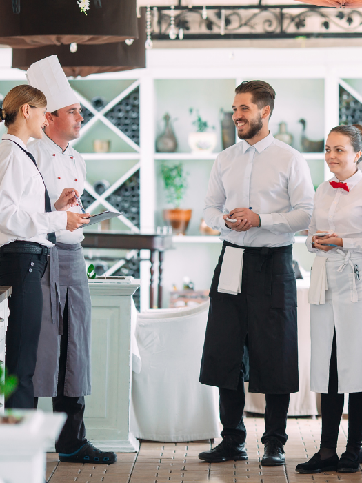 Personal de restaurante participando en una sesión de formación integral, aprendiendo técnicas variadas que van desde la manipulación de alimentos hasta la atención al cliente, en un entorno elegante de restaurante.