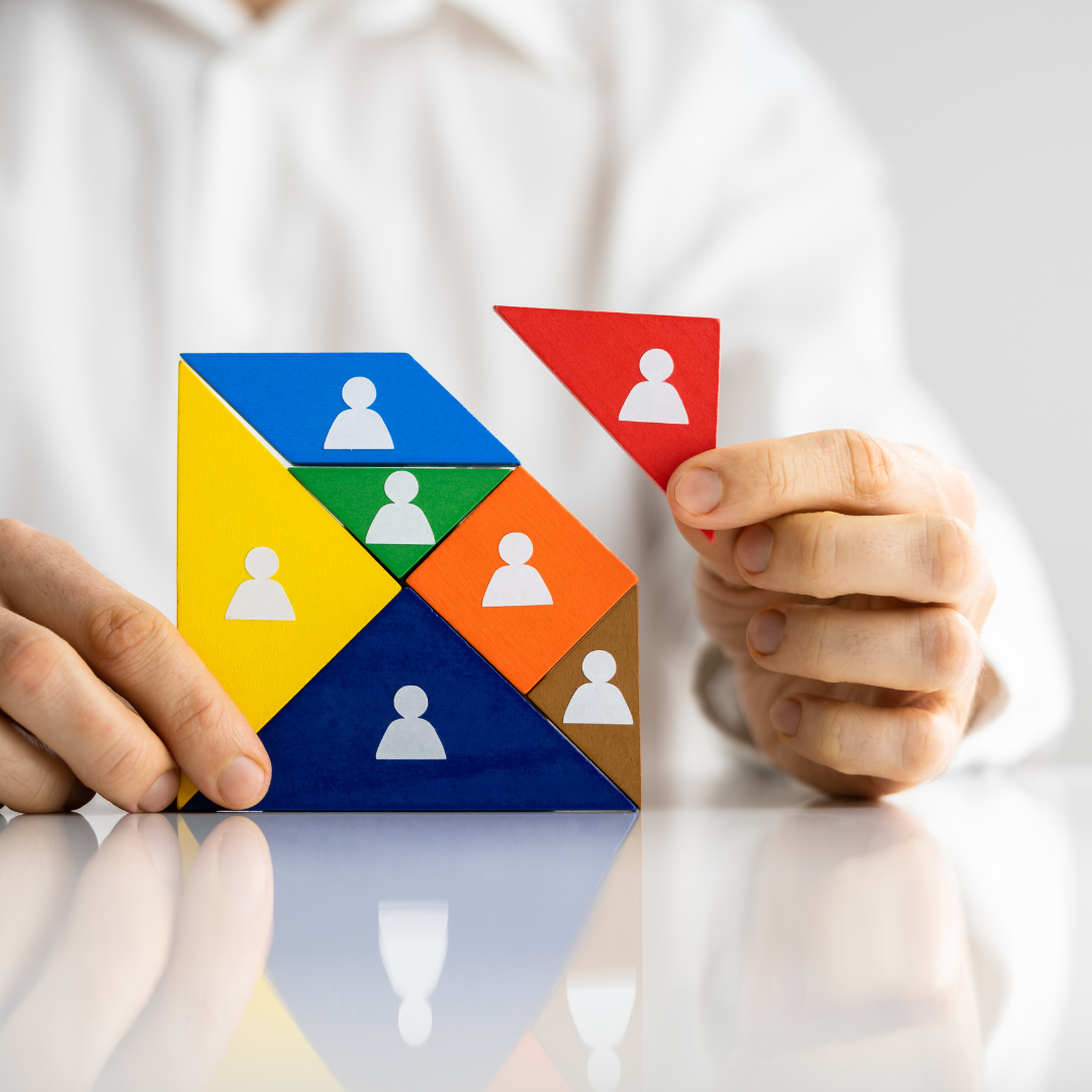 Manos construyendo una figura de equipo con bloques de colores, cada uno representando personas o roles distintos. Transmite estrategia, estructura y selección precisa.
